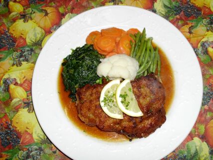 Ein Teller mit paniertem Schnitzel, gr&uuml;nen Bohnen, Karotten, Blumenkohl und Spinat, garniert mit Zitronenscheiben, serviert im Hotel-Restaurant zum Wilden Mann.