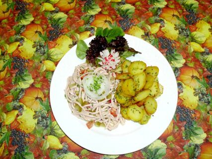 Ein Teller mit einem Gericht aus Kartoffelscheiben, Wurstsalat und Salatbl&auml;ttern auf einem herbstlich gemusterten Tischtuch im Hotel-Restaurant zum Wilden Mann.