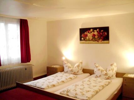 Gem&uuml;tliches Doppelzimmer mit floral gemusterter Bettw&auml;sche und roten Vorh&auml;ngen im Hotel-Restaurant zum Wilden Mann.