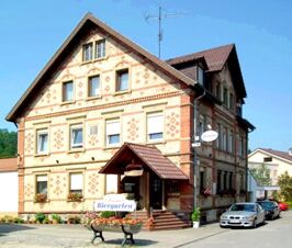 Three-story brick building with a pitched roof, entrance canopy, sign for Biergarten, and Gasthof Lamm Hotel und Restaurant name visible