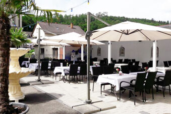 Outdoor dining area with black chairs, white tablecloths, large umbrellas, and a fountain at Gasthof Lamm Hotel und Restaurant