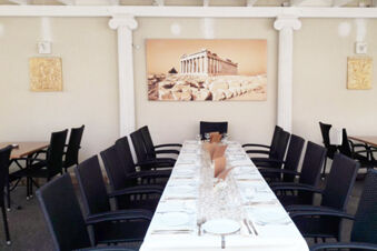 Long table with white tablecloth, glassware, and cutlery set for twelve in Gasthof Lamm Hotel und Restaurant dining area with wall art
