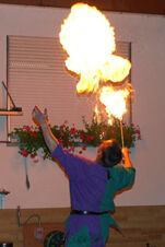 A performer at Gasthof Lamm Hotel und Restaurant blows fire from a torch creating large flames near a window with flower boxes