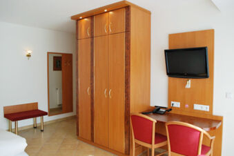 Hotel room at Gasthof Lamm Hotel und Restaurant with wooden wardrobe, two red chairs, wall-mounted TV, desk, mirror, and a bench