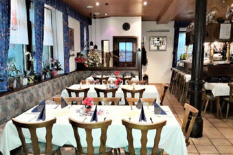 Dining area with wooden chairs and tables set with white tablecloths, napkins, and flowers at Gasthof Lamm Hotel und Restaurant