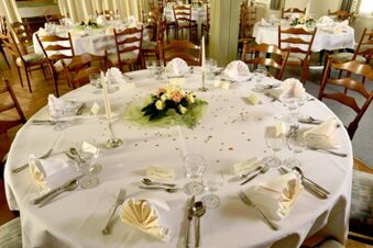 Feestelijk gedekte tafels met witte wijn- en waterglazen, servetten en bloemdecoraties in het restaurant van Gasthof Basedau.
