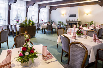 Licht en uitnodigend restaurant in Gasthof Basedau met gedekte tafels, bloemendecoraties en een gezellige open haard op de achtergrond.