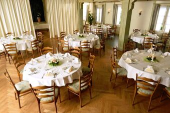 Licht ingerichte eetzaal met ronde tafels, witte tafelkleden en decoraties in Gasthof Basedau, ideaal voor feestelijke gelegenheden.