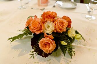 Bloemstuk met oranje rozen en witte bloesem op een gedekte tafel in Gasthof Basedau voor een feestelijke decoratie.