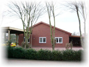 ホテル＆アパルトマン クロステルマンの赤レンガのファサードは、2つの窓と駐車スペースがあるシンプルな家屋で、周囲は木々や低木に囲まれている。