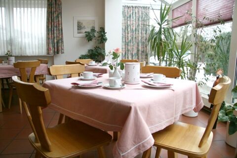 Salle de petit-d&eacute;jeuner lumineuse avec des nappes roses et des meubles en bois, d&eacute;cor&eacute;e de fleurs, dans la pension Garni Zweck.