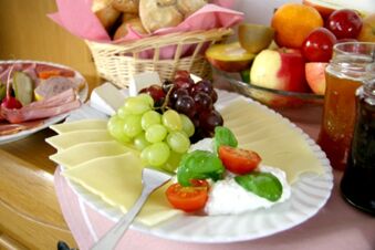 Table de petit-d&eacute;jeuner avec plateau de fromages, raisins, tomates, charcuterie, pain et confiture dans l'offre de la pension Garni Zweck.