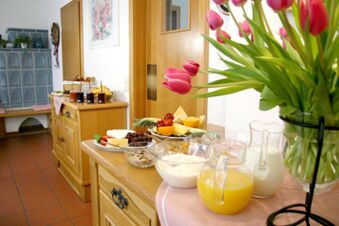 Petit d&eacute;jeuner buffet avec fruits frais, jus de fruits et yaourts dans une salle confortable de la Pension Garni Zweck d&eacute;cor&eacute;e de tulipes.