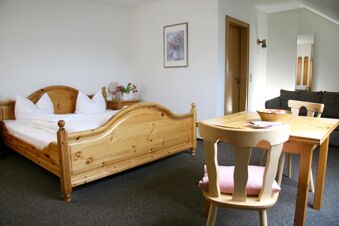 A simple wooden double bed and matching bedside table with pink flowers, wooden table and chairs in Pension Garni Zweck room