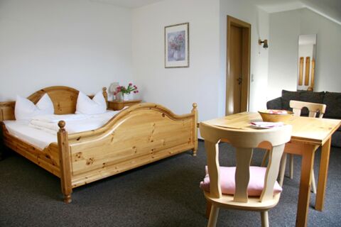 A simple wooden double bed and matching bedside table with pink flowers, wooden table and chairs in Pension Garni Zweck room