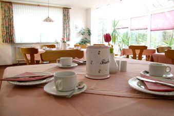Salle de petit-d&eacute;jeuner lumineuse avec tables et tasses &agrave; caf&eacute; dress&eacute;es dans la pension Garni Zweck avec nappes roses.
