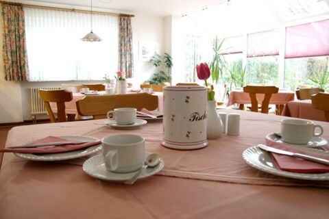 Salle de petit-d&eacute;jeuner lumineuse avec tables et tasses &agrave; caf&eacute; dress&eacute;es dans la pension Garni Zweck avec nappes roses.