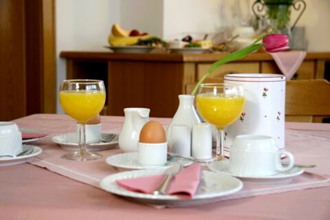 Petit-d&eacute;jeuner sur table avec jus d'orange, &oelig;uf &agrave; la coque, caf&eacute; et une tulipe sur une table de la pension Garni Zweck.