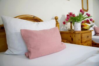 Bed with white pillow and pink cushion next to a wooden nightstand holding a vase of pink tulips at Pension Garni Zweck