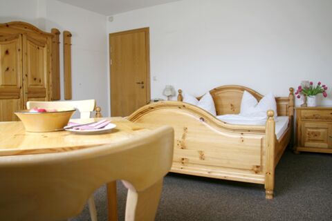 Wooden double bed with white pillows and blankets, wooden wardrobe, table with bowl of apples, and chair at Pension Garni Zweck