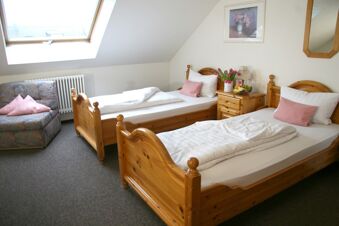 Two single wooden beds with white linens and pink pillows in a bright room at Pension Garni Zweck with a floral armchair and nightstand