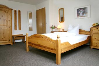 Bedroom with wooden bed, wardrobe, dresser, and a nightstand with a lamp and flowers at Pension Garni Zweck