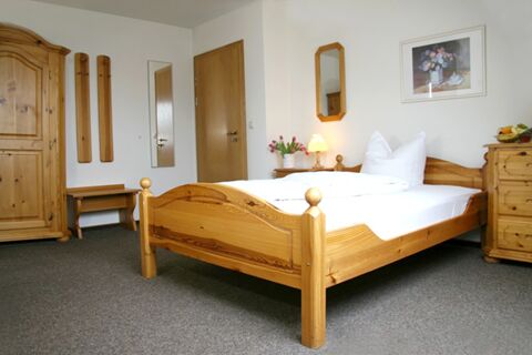 Bedroom with wooden bed, wardrobe, dresser, and a nightstand with a lamp and flowers at Pension Garni Zweck