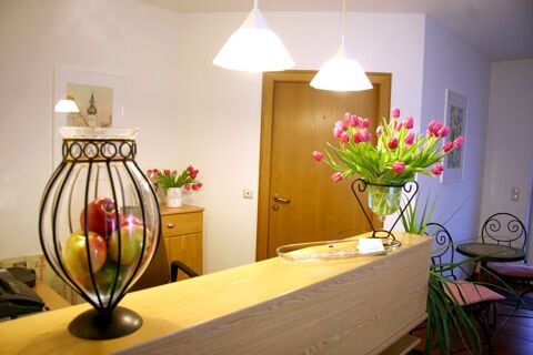 Wooden reception desk with metal fruit bowl holding apples and a vase of pink tulips at Pension Garni Zweck lobby