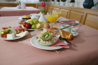Table de petit-d&eacute;jeuner avec fruits frais, petits pains, charcuterie, fromage et jus d'orange dans l'atmosph&egrave;re du petit-d&eacute;jeuner de la pension Garni Zweck.