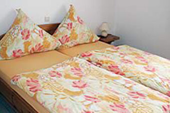 Gem&uuml;tliches Doppelbett mit bunten Bettdecken in einem schlichten Zimmer bei Ferienwohnungen G&auml;stehaus Therme-Blick.