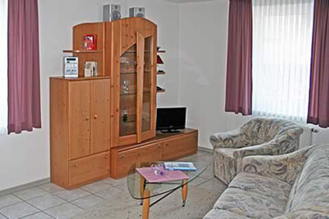 Gem&uuml;tlicher Wohnbereich mit Sofa, Sessel, Glastisch und Holzm&ouml;beln in einer Ferienwohnung im G&auml;stehaus Therme-Blick.