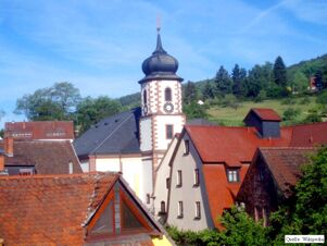 Au&szlig;enansicht eines historischen Geb&auml;udekomplexes mit Kirchturm und roten Ziegeld&auml;chern bei Elke's Landgasthof Zum Anker Partyservice Elke Bauer unter blauem Himmel.