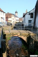 Blick auf eine kleine malerische Br&uuml;cke &uuml;ber einen Bach mit umliegenden H&auml;usern und Kirchturm, typisch f&uuml;r Elke's Landgasthof Zum Anker Partyservice Elke Bauer.