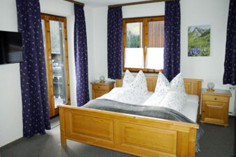 Bedroom with wooden bed, nightstands, purple curtains, a wall-mounted TV, and a balcony at Bauernhof Ferienhof K&uuml;hberg