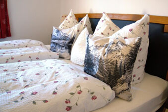 Double bed with floral and mountain print bedding and pillows at Bauernhof Ferienhof K&uuml;hberg
