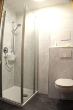 Shower enclosure with glass doors and wall-mounted showerhead next to a wall-mounted toilet in a Bauernhof Ferienhof K&uuml;hberg bathroom