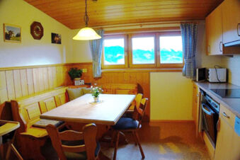 Dining area with wooden table, chairs, bench, a kitchen with oven and microwave, and windows at Bauernhof Ferienhof K&uuml;hberg