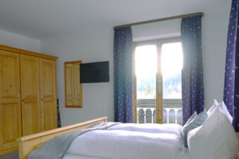 Bedroom interior at Bauernhof Ferienhof K&uuml;hberg with wooden wardrobe, double bed, window with blue curtains and TV mounted on wall