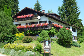 White multi-story house with flower-filled balconies surrounded by trees and a garden at Bauernhof Ferienhof K&uuml;hberg
