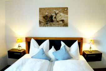 Double bed with white and blue pillows, two bedside tables with lamps, and a cow picture above at Bauernhof Ferienhof K&uuml;hberg
