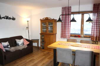 Living room at Bauernhof Ferienhof K&uuml;hberg with a brown sofa, wooden cabinet, dining table, and plaid curtains on the window