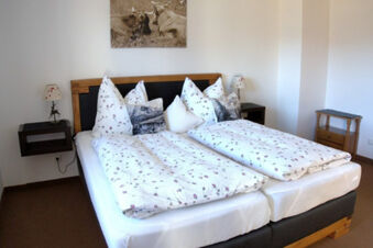 Double bed with floral bedding and decorative pillows, wooden headboard, nightstands with lamps in Bauernhof Ferienhof K&uuml;hberg bedroom
