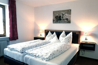Double bed with white floral bedding between two wooden nightstands with lit lamps in Bauernhof Ferienhof K&uuml;hberg bedroom
