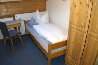 Simple bedroom interior at Bauernhof Ferienhof K&uuml;hberg with a single wooden bed, two pillows, wooden wardrobe, and small desk with chair