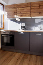 Modern kitchen with wooden upper cabinets, dark lower cabinets, a coffee maker, and oven at Bauernhof Ferienhof K&uuml;hberg