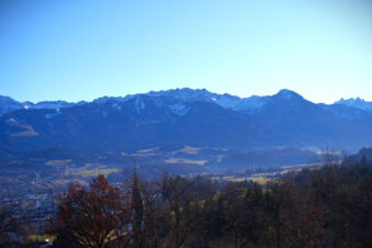 Mountain range with snow patches under blue sky viewed from a valley with trees in foreground at Bauernhof Ferienhof K&uuml;hberg