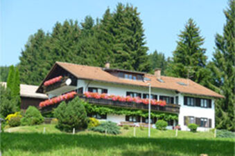 White multi-story house with flower-filled balconies surrounded by greenery and trees at Bauernhof Ferienhof K&uuml;hberg