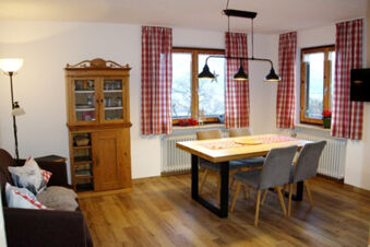 Dining area with wooden table, four gray chairs, wooden cabinet, lamp, sofa, and red checkered curtains at Bauernhof Ferienhof K&uuml;hberg