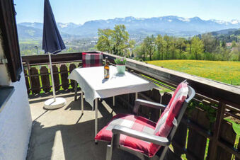 Balcony with two chairs with red cushions, a table with a white cloth and a bottle at Bauernhof Ferienhof K&uuml;hberg overlooking mountains and green fields