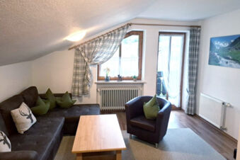Living area with brown sofa, green pillows, wooden coffee table, black armchair, window, and curtains at Bauernhof Ferienhof K&uuml;hberg